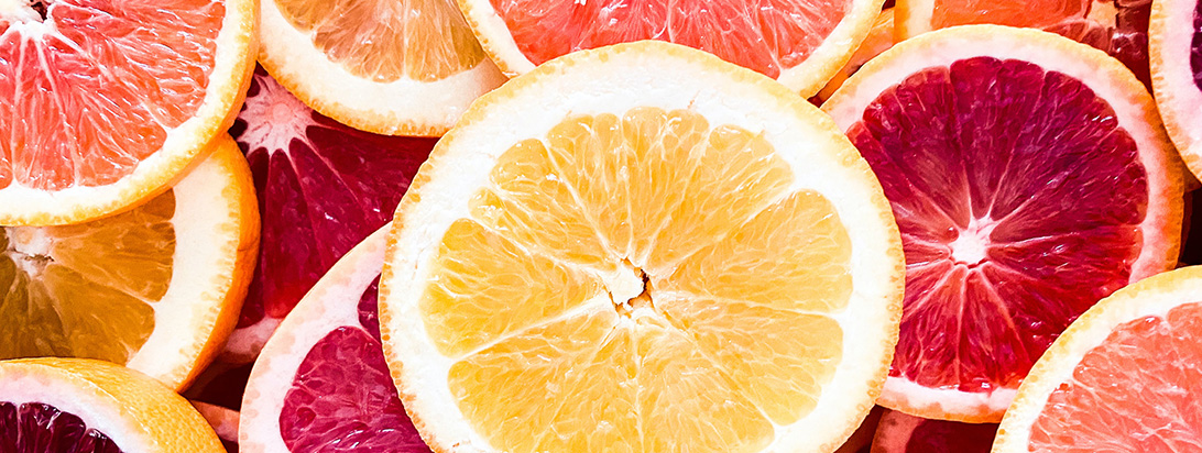 A close-up of vibrant, overlapping slices of red, pink, and yellow grapefruit.
